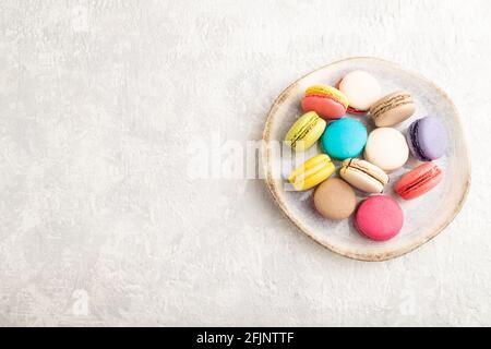 Multicolored macaroons on ceramic plate on gray concrete background. top view, copy space, still life. Breakfast, morning, concept. Stock Photo