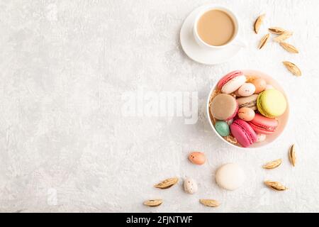 Multicolored macaroons and chocolate eggs in ceramic bowl, cup of coffee on gray concrete background. top view, copy space, still life. Breakfast, mor Stock Photo