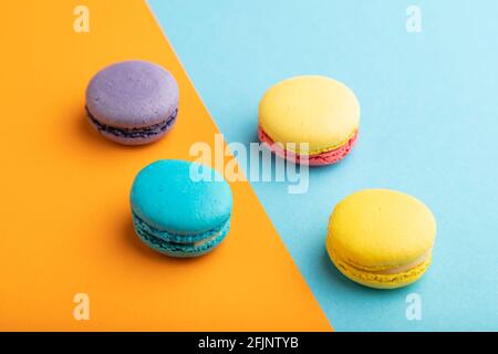 Yellow, purple and blue macaroons on blue and orange pastel background. side view, close up. Minimalism, morning, contrast concept. Stock Photo