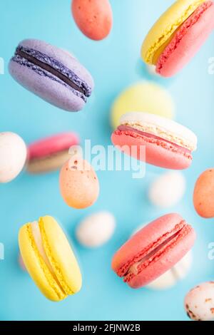 Multicolored flying macaroons and chocolate eggs frozen in the air on blurred blue background. top view, flat lay, close up. Breakfast, morning, conce Stock Photo