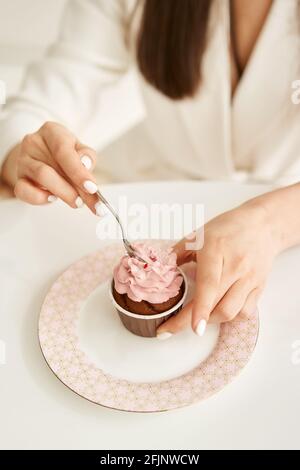 woman eating pink cupcake on the plate, by little spoon Stock Photo