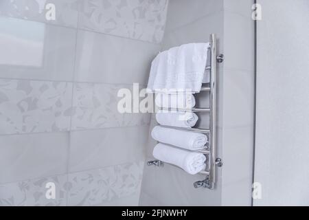 On an iron metal dryer holder, there are white terry towels for the shower. Hygiene, cleanliness concept. Marble tiles background in the bathroom. Tre Stock Photo