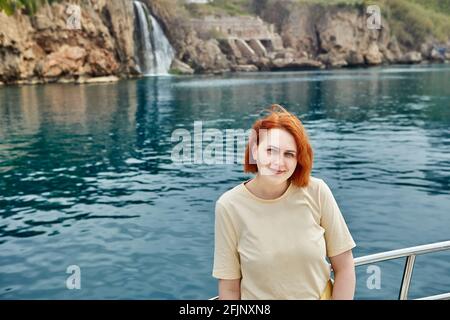 Tourist yacht sails past small waterfall, young European woman poses for photo. Stock Photo