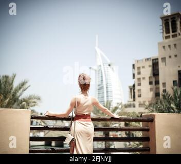 Happy beautiful unrecognizable back tourist woman in summer dress enjoying hotel Burj al Arab in Dubai in United Arab Emirates