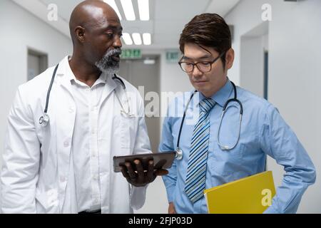 Couple of diverse male doctors walking through corridor looking at tablet Stock Photo