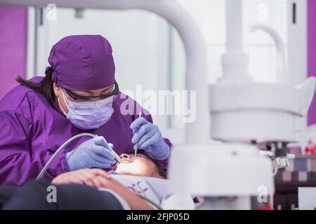 A closeup of a Mexican female dentist doing dental treatment on the young girl Stock Photo
