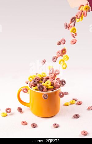 colored cereal rings falling into an orange cup on white background with side lighting Stock Photo