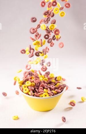 colored cereal rings falling into a yellow bowl on white background with soft side lighting Stock Photo