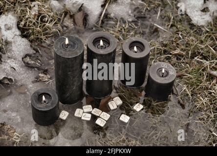 Grunge still life with black candles and runes in water outside. Esoteric, gothic and occult background, Halloween mystic and wicca concept outdoors. Stock Photo