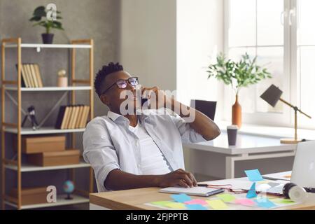 Young Afro American businessman sitting at office desk and talking on mobile phone Stock Photo