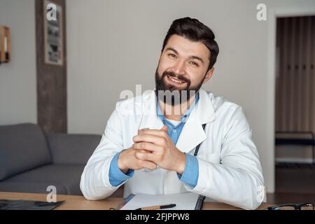 Happy smiling young caucasian doctor in medical coat looking at camera Stock Photo