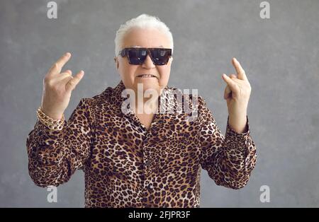 Steep mature man shows a rock sign with both hands standing on a gray background. Stock Photo