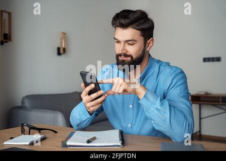 Millennial caucasian man freelancer with smartphone sitting at home office desk Stock Photo