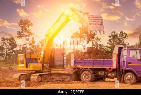 Backhoe working by digging soil at construction site and loading to the truck. Bucket of backhoe transport soil to truck. Crawler excavator dump dirt Stock Photo