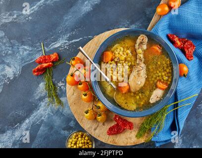 Pea soup with chicken, carrots, tomatoes and herbs in a deep plate on wooden board with napkin on blue background Stock Photo