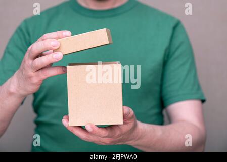 A man dressed in green t-shirt holding small paper cardboard box with open cap Stock Photo