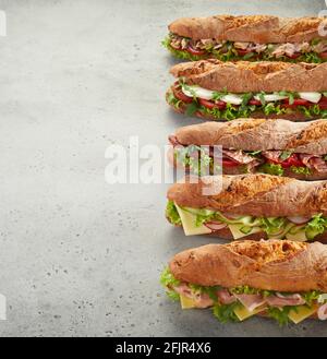 From above bunch of tasty sub sandwiches made of vegetables with meat and cheese and placed in row on side of gray table Stock Photo