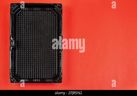 Empty rectangular black plastic container for products on a red background. Plastic container for sushi set delivery. Take away lunch box. Top view. F Stock Photo