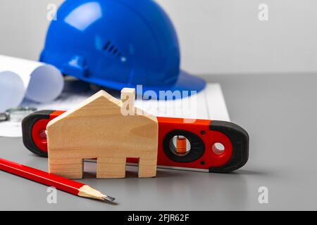 Wooden house model, blueprints and building level on gray desk Stock Photo