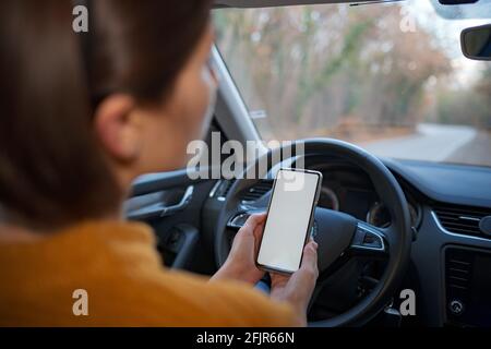 Mockup image of a woman holding and using mobile phone with blank screen while driver a car. People, Driving, Navigation and Transportation Concepts Stock Photo