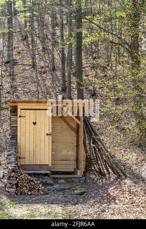 Rustic wooden toilet in the forest with a heart-shaped hole in the door boards. Wooden outhouse in the nature. Stock Photo