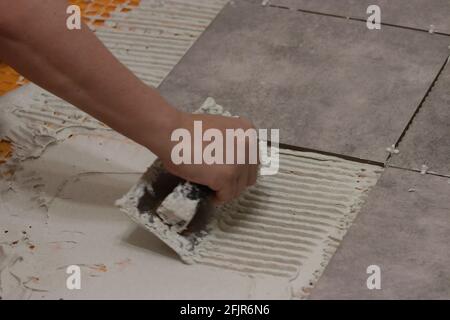 womans hand laying down thinset to tile a floor Stock Photo
