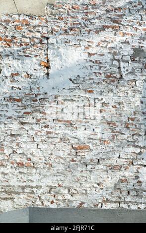 A whitewashed grungy brick wall with the red bricks visible in places in sunlight with shadow. Stock Photo
