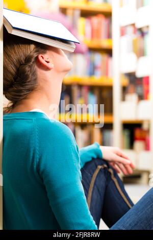 Student - Young woman in library with book learning, she is asleep Stock Photo