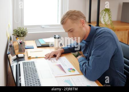 Pensive young entrepreneur checking and analyzing information in financial documents on his office desk Stock Photo