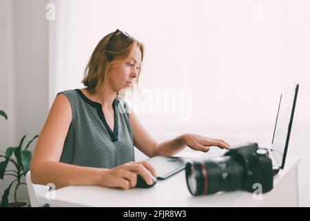 Young caucasian woman using digital graphic tablet and drawing pen to retouch the images. Stock Photo