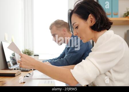 Team of young business people proofreading and checking project documents and reports Stock Photo