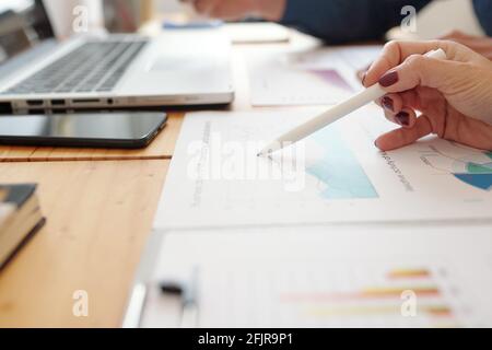 Close-up image of female entrepreneur pointing at chart with sales statistics on her desk Stock Photo