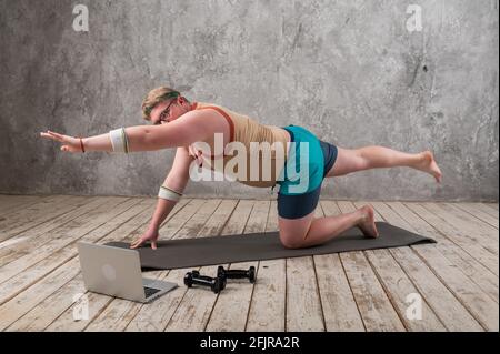 Funny fat man in sportswear doing sports exercises looking into a laptop. home workout  Stock Photo