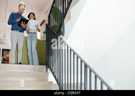 Young entrepreneurs standing on steps and discussing details of project plan Stock Photo