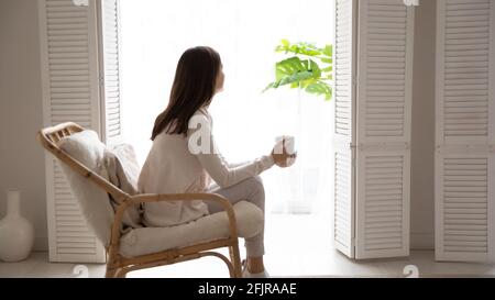 Peaceful relaxed girl enjoying morning cup of coffee in armchair. Stock Photo