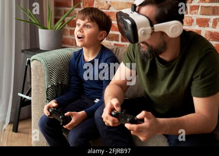 Father wearing VR glasses playing with son at home Stock Photo