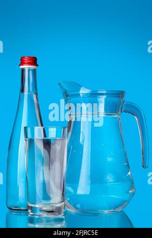 glassware filled with clean drinking water for health objects glass and jug with handle and bottle with lid still life on a blue background. Stock Photo