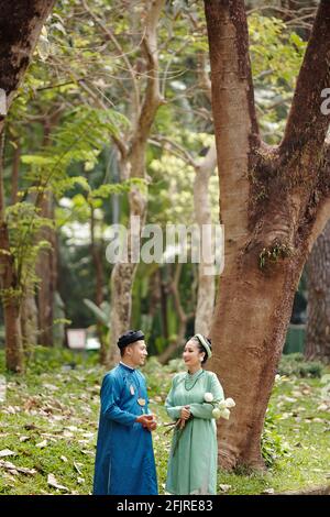Happy bride and groom in traditional Vietnamese costumes talking in park after having wedding ceremony Stock Photo