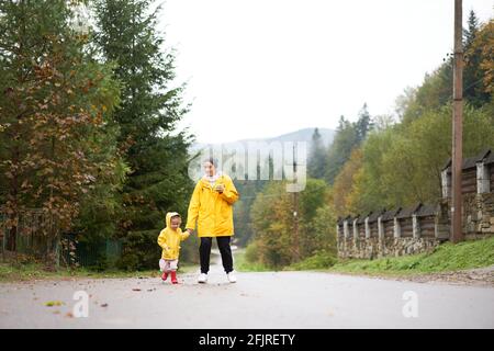 Rainy day Mother and little daughter walking after rain dressed yellow raincoat Happy family with one child. Positive emotions Stock Photo