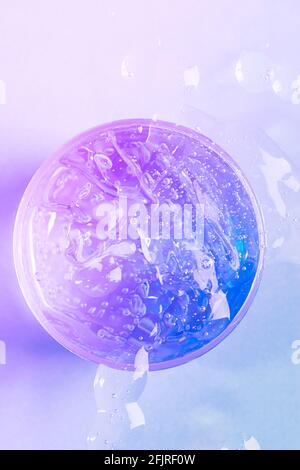 Cosmetic liquid gel serum lubricant hyaluronic acid with oxygen bubbles on purple neon background. Hair, body or face care. Flat design top view cosme Stock Photo