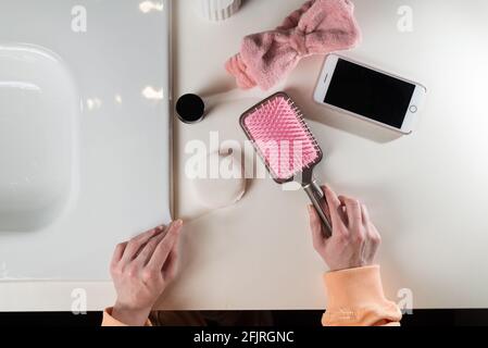 top view of bathroom accessories, toothbrush near hair brush, bow, mobile phone and face sponge on a white surface Stock Photo