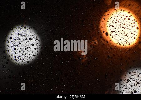 Bokeh photo of lights behind a wet car window during a rainy night. Stock Photo