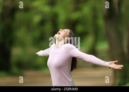 Excited woman outstretching arms and screaming in a forest celebrating ...