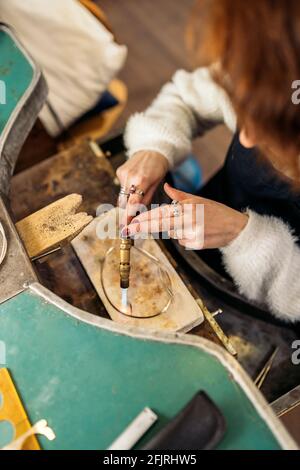 Stock photo of faceless woman using blowtorch in jewelry workshop. Stock Photo