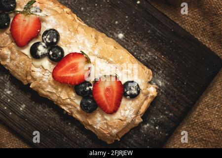 Meringue cake with fresh strawberries and blueberries on a black cutting board Stock Photo