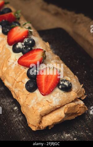 Meringue cake with fresh strawberries and blueberries on a black cutting board Stock Photo