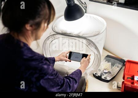 Faceless craftswoman using her mobile phone in jewelry workshop to take photo. Stock Photo