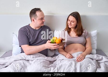 A man gives a pregnant woman a tray with a plate of fruit - the concept of proper nutrition during pregnancy, weight control Stock Photo