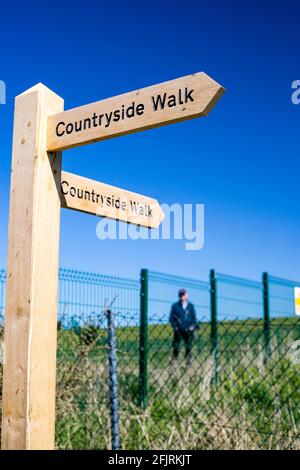 A signpost depicting countryside walks with a male walker in the background on a bright spring day in Oxfordshire Stock Photo