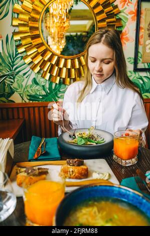 Young beautiful woman have business lunch in cafe. Beautiful luxury interior, golden and green colors. Stock Photo